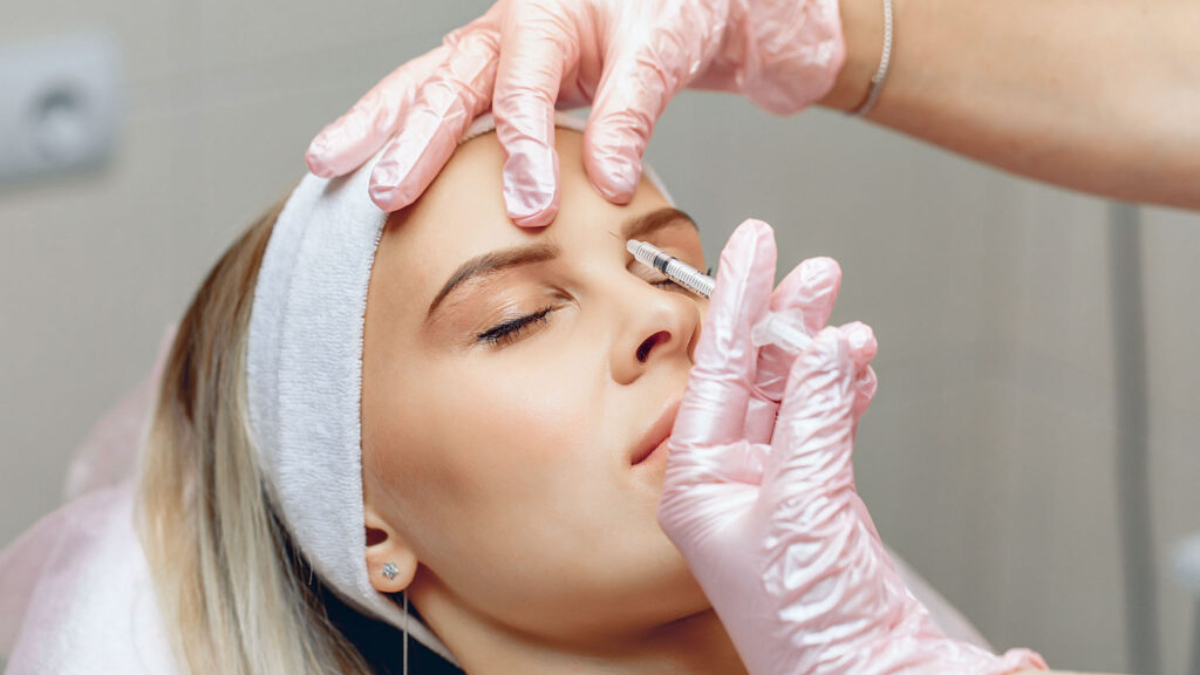 Neat master beautician who injects Botox in the brow area of ​​a beautiful, charming patient. Anti-aging treatment concept